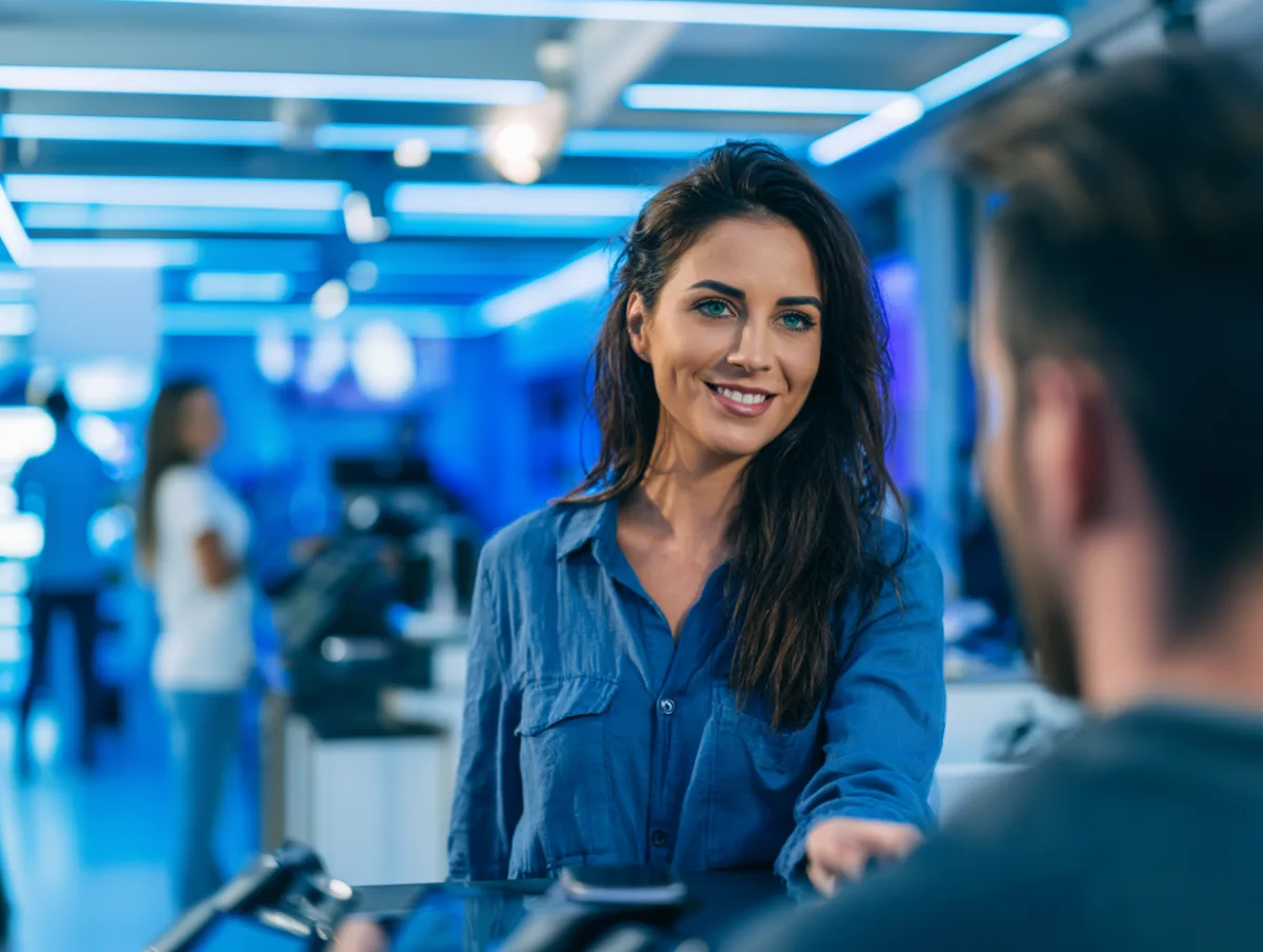 Wireless store employee handing a customer a smartphone at the counter of a prepaid phone shop.